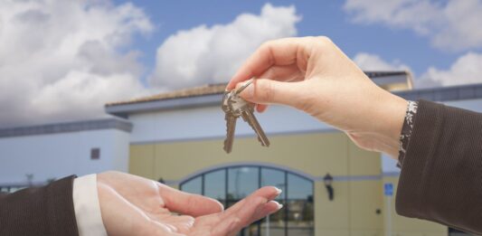How A Mortgage Broker Can Help When Buying Business Property Real Estate Agent Handing Over the Keys in Front of Vacant Business Office.
