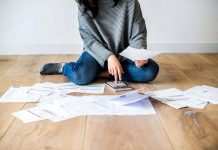 Managing Your Business Finances Before Day One Is Possible A woman sitting on the floor surrounded by sheets of paper using a calculator.