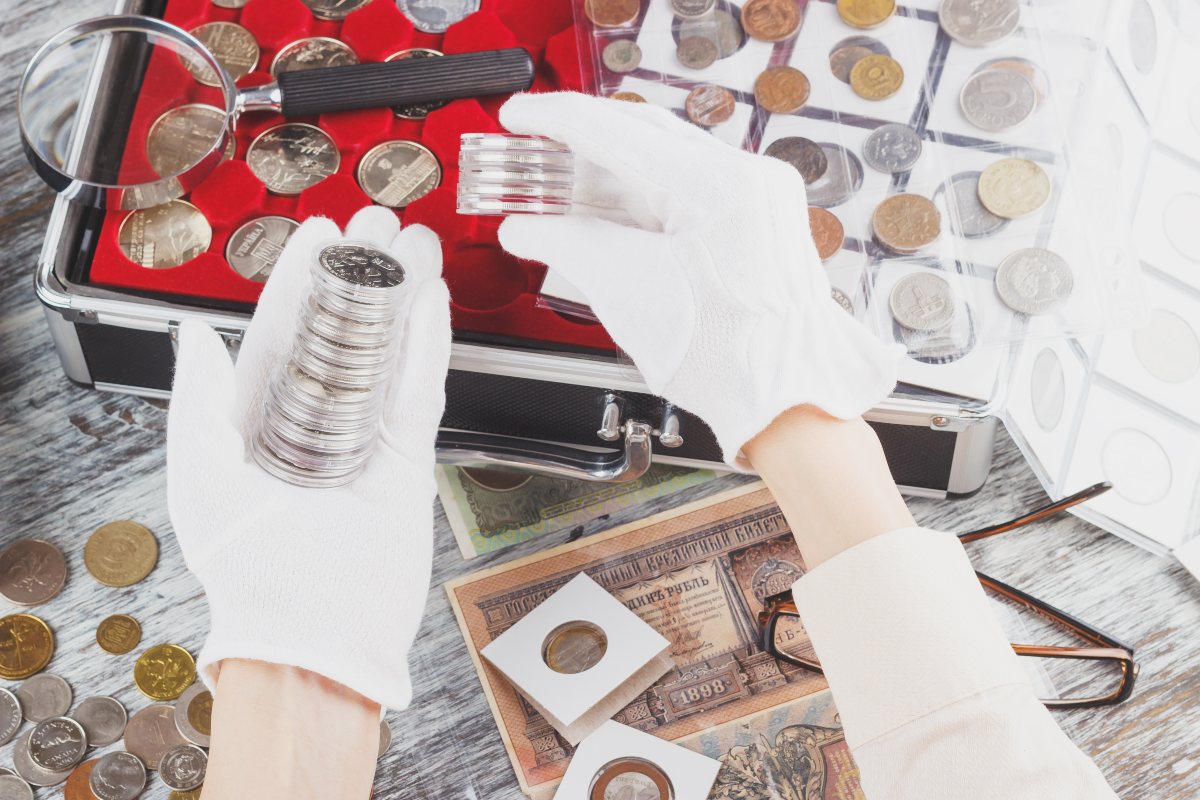 Hands in the white gloves with different collector coins in the boxes, top view